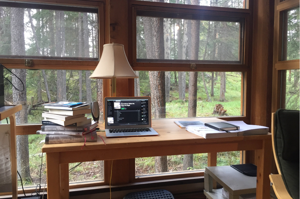 Mesa de trabajo con proyectos literarios impresos, notas de evaluación y una taza de café en Banff, Canadá